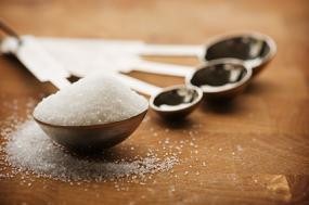 Close up of a tablespoon filled with sugar resting on a wooden countertop